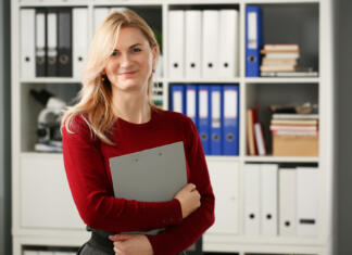 Happy smiling blond businesswoman holdig gray folder in hand office workplace look at camera