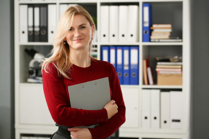 Happy smiling blond businesswoman holdig gray folder in hand office workplace look at camera