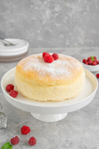Japanese cotton cheesecake on a stand on a gray concrete background with fresh raspberries and powdered sugar on top. Selective focus, copy space