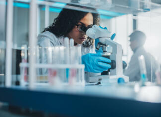 Univerza na Primorskem išče nove mlade raziskovalce! Medical Science Laboratory: Portrait of Beautiful Black Scientist Looking Under Microscope Does Analysis of Test Sample. Ambitious Young Biotechnology Specialist, working with Advanced Equipment