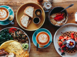 Morning breakfast on a table above, waffles with cream, berries, coffee, cappuccino, bowl, omlet with vegetables, bread with butter, avocado cream, vegan food, healthy food, meal.