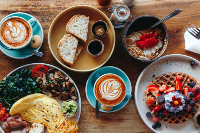 Morning breakfast on a table above, waffles with cream, berries, coffee, cappuccino, bowl, omlet with vegetables, bread with butter, avocado cream, vegan food, healthy food, meal.