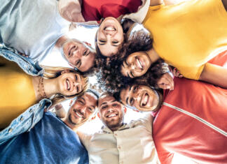 Zakaj je socialni kapital tako pomemben? Multiracial group of young people standing in circle and smiling at camera - Happy diverse friends having fun hugging together - Low angle view