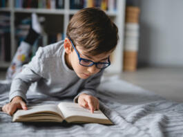 One caucasian boy lying on the floor at home in day reading a book front view copy space real people education concept