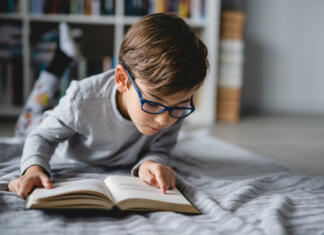 Najboljše knjige za mladostnike One caucasian boy lying on the floor at home in day reading a book front view copy space real people education concept
