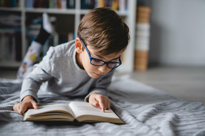 One caucasian boy lying on the floor at home in day reading a book front view copy space real people education concept