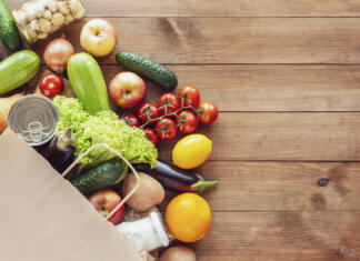 Hrana na recept zdravilo prihodnosti? Zdravniki predpisali zastonj hrano kot eksperiment Paper grocery bag with fresh vegetables, fruits, milk and canned goods on wooden backdrop. Food delivery, shopping, donation concept. Healthy food background. Flat lay, copy space.
