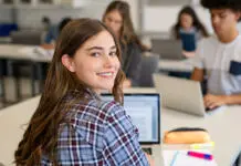 Študent, ne pozabi – Poteka drugi prijavni rok za vpis na faks Portrait of smart university student in library with classmates in background. Close up face of school girl looking at camera while studying on computer. Smiling young woman looking behind while studying on laptop in university library.