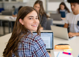 Študent, ne pozabi – Poteka drugi prijavni rok za vpis na faks Portrait of smart university student in library with classmates in background. Close up face of school girl looking at camera while studying on computer. Smiling young woman looking behind while studying on laptop in university library.