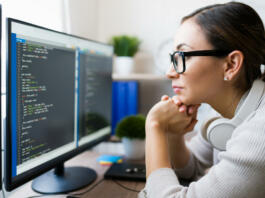 Profile of a hispanic freelancer wearing glasses and reading the coding software on the computer. Focused programmer checking the app code