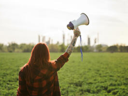 Rear view of young woman activist with megaphone standing outdoors by oil refinery, protesting.