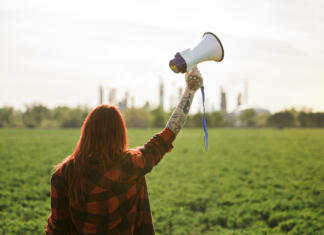 Komentar: Podnebje potrebuje boljše aktiviste Rear view of young woman activist with megaphone standing outdoors by oil refinery, protesting.