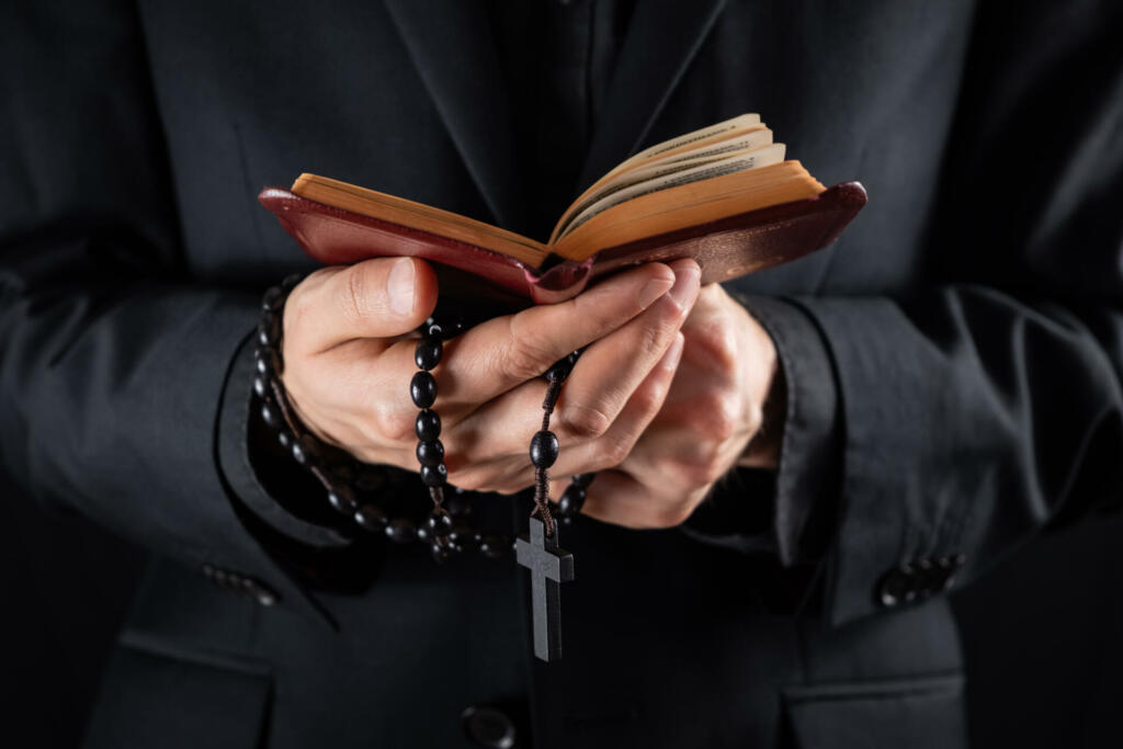 Religious person studies Bible and holds prayer beads, low-key image