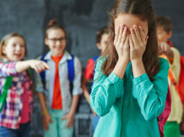 Schoolgirl crying on background of classmates teasing her