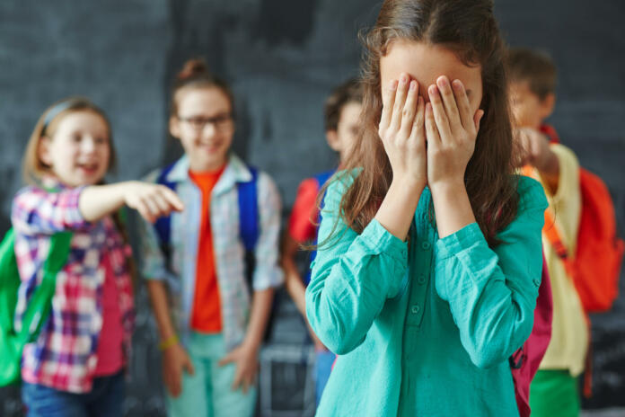 Schoolgirl crying on background of classmates teasing her