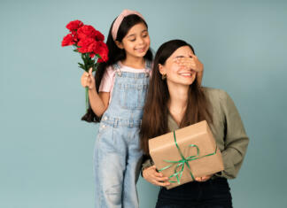 Materinski dan: Kako je nastal materinski dan in zakaj ga praznujemo? Surprise! Adorable young daughter covering her mom's eyes and surprising her with a birthday gift