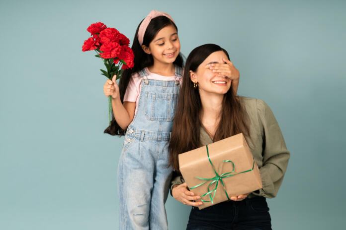 Surprise! Adorable young daughter covering her mom's eyes and surprising her with a birthday gift