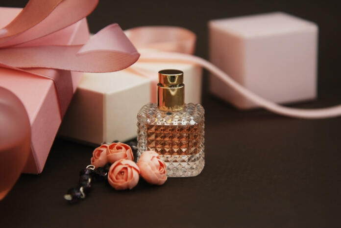 Women's Pink Perfume in Beautiful Bottle and Artificialt Flowers Bracelet on Brown Background with gift boxes.