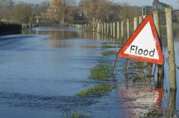 A flood warning sign, on a closed country road next to water logged fields in the Avon Valley, Hampshire, England. Flooded after an extreme amount of rainfall at the start of 2014