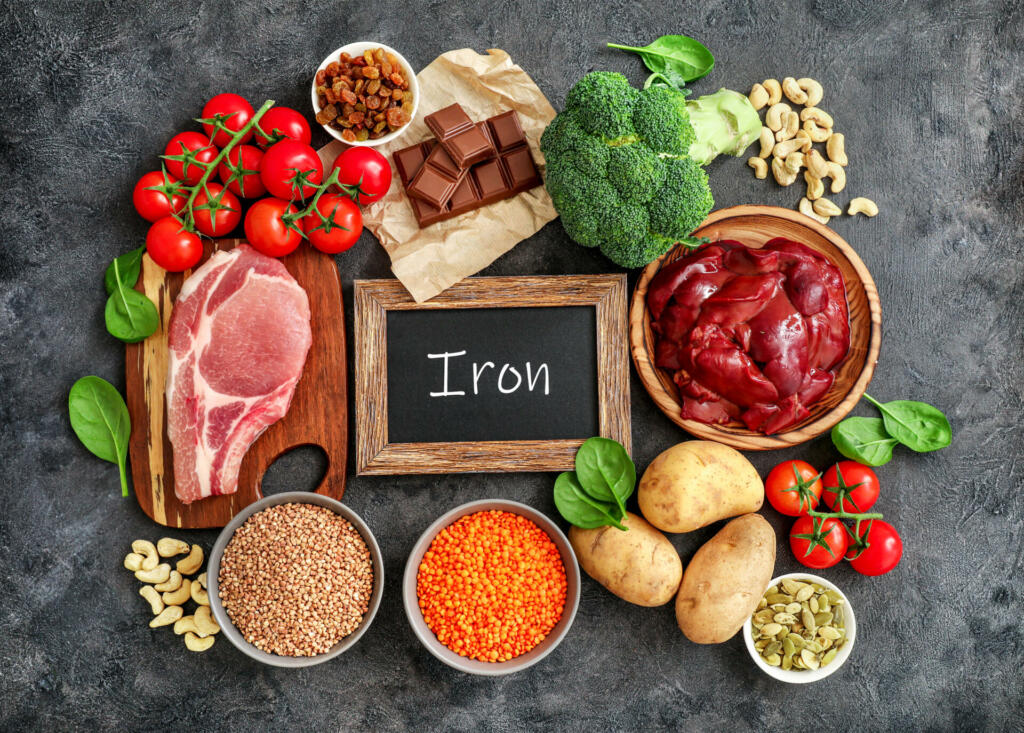 Assortment of high in Iron sources on dark background: liver, beef, raisins, keshew, buckwheat, spinach, tomatoes, potatoes, dark chocolate, pumpkin seeds, lentil, broccoli. Top view.