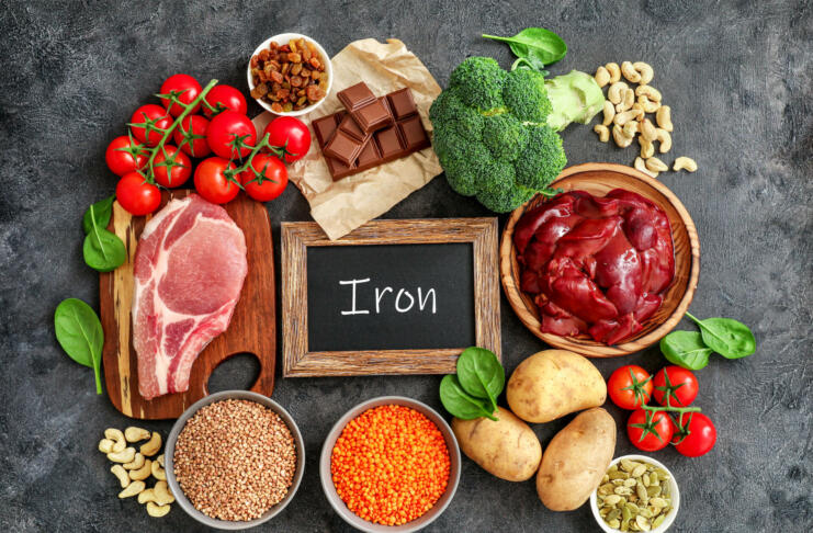 Assortment of high in Iron sources on dark background: liver, beef, raisins, keshew, buckwheat, spinach, tomatoes, potatoes, dark chocolate, pumpkin seeds, lentil, broccoli. Top view.