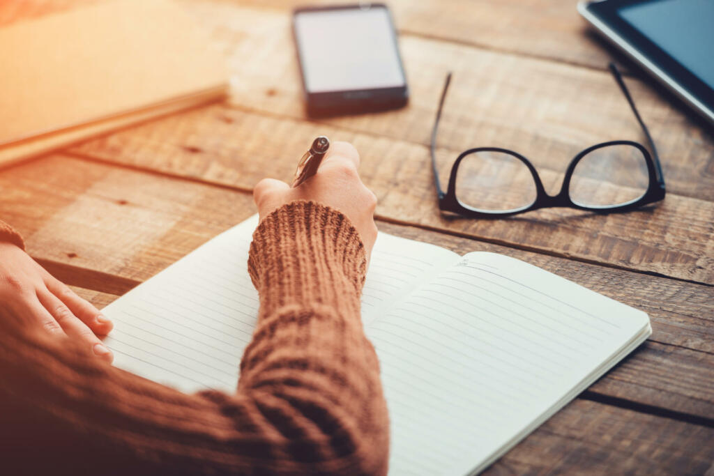 Close-up image of woman writing in notebook with copy space while sitting at the rough wooden table