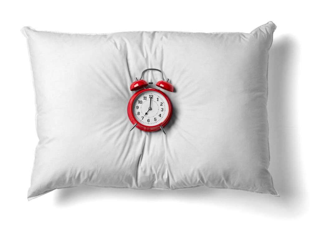 close up of a white pillow and red alarm clockon white background