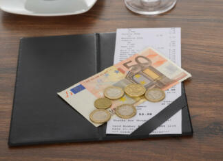 Koliko napitnine moraš pustiti v Sloveniji in drugih državah? Close-up Of Bill With Euro Note On Wooden Table