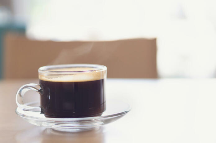 Closeup glass of hot americano coffee on wood table with smoke, selective focus, vintage tone