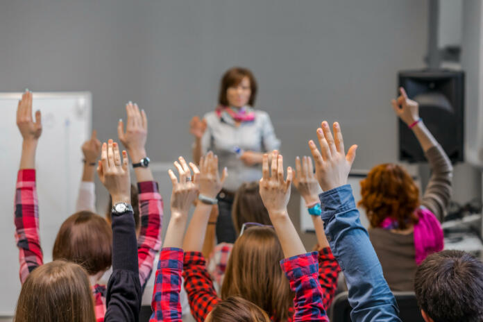 Diverse Group of Students in Conference Room raising Arms up actively participating in Seminar Teachers Body on background