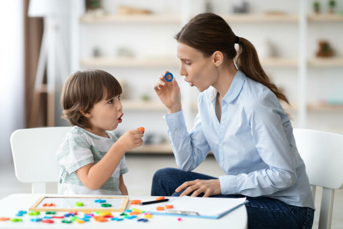 Female speech therapist curing child's problems and impediments. Little boy learning letter O with private English language tutor during lesson at office