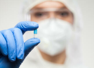 Zaviralci pubertete: Kaj vemo o tej skupini zdravil? Female UK NHS pharmacist wearing PPE personal protective equipment,coveralls,face mask,eyewear,glove,holding blue pill,selective focus,patient cure remedy for illness disease,prescription drug concept