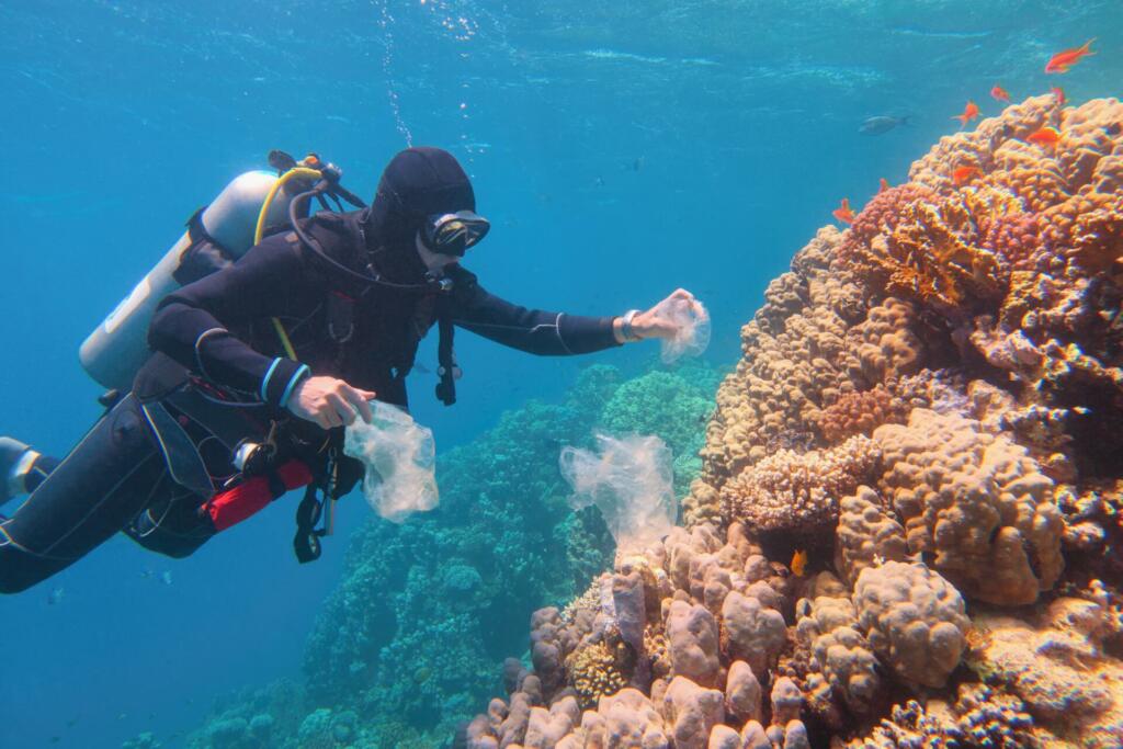 Man scuba diver cleaning plastic  from the tropical coral reef. World ocean contaminated by plastic. Environment pollution concept.