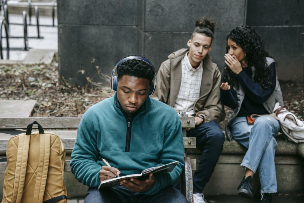 Multiracial students gossiping about black man with notepad