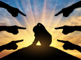 Peers' hands show with their fingers a sad and frightened child girl against the sunset. Conceptual image of bullying children