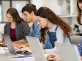 Serious college students studying on laptop sitting in a row in library. Young university multiethnic students using computer for study in classroom. Side view of casual girl typing on laptop during computer lesson.