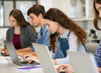Prepis iz ene srednje šole na drugo – realnost ali utopija? Serious college students studying on laptop sitting in a row in library. Young university multiethnic students using computer for study in classroom. Side view of casual girl typing on laptop during computer lesson.