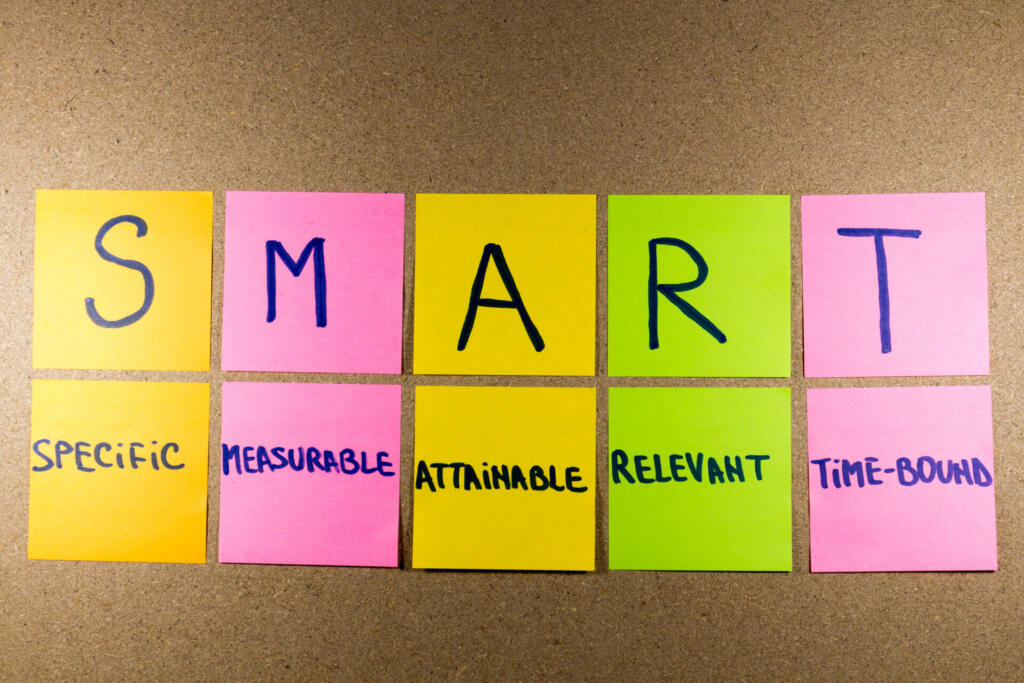 set goals SMART (specific, measurable, attainable, recorded, timely) colorful sticky notes on cork bulletin board