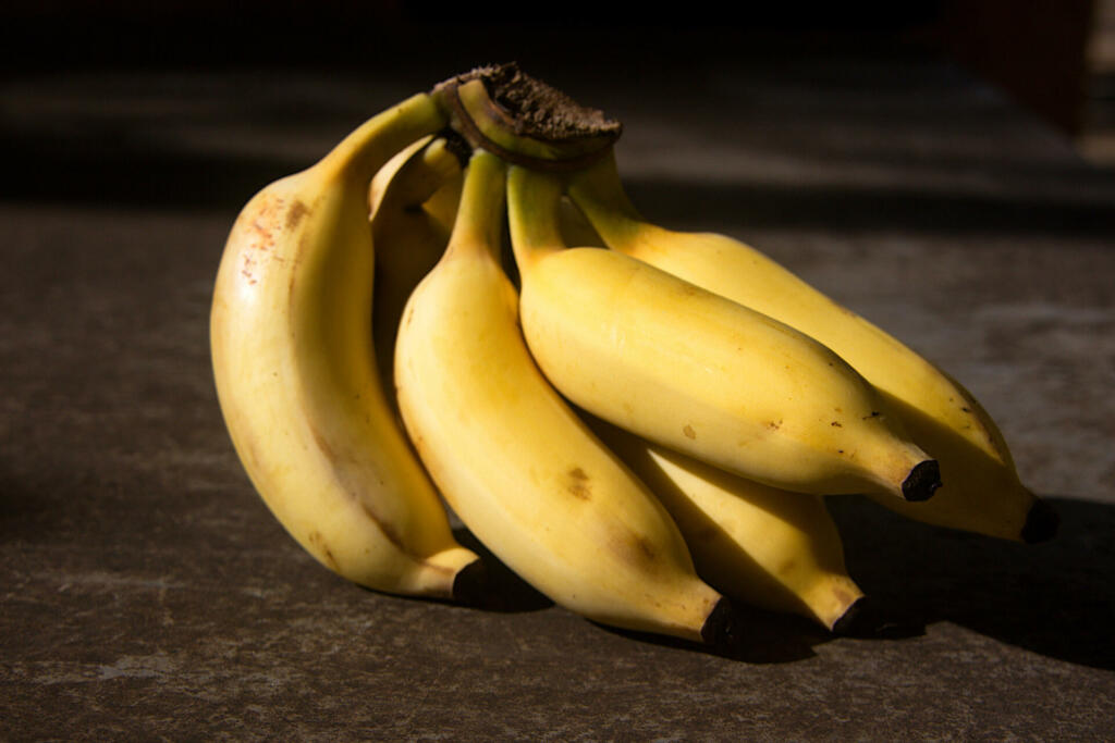 Small cluster ripe, yellow bananas placed on floor in sunlight