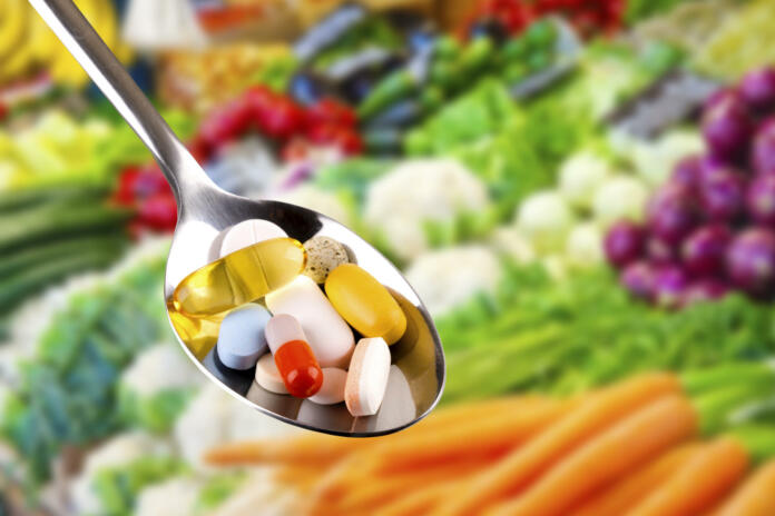 spoon with variety of pills, dietary supplements on blurred vegetables background