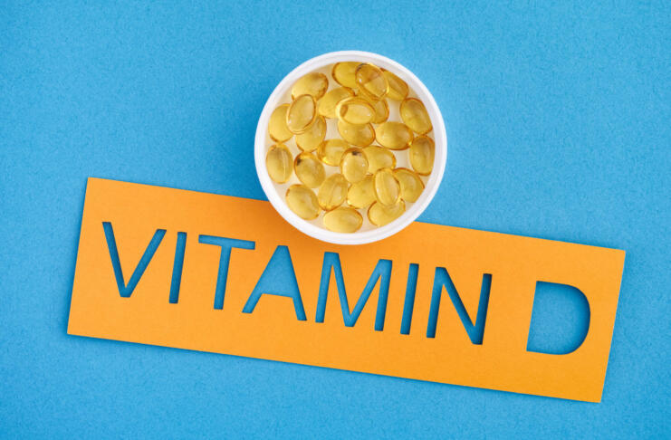 The word Vitamin D with a small cup of Vitamin D3 capsules on it. Close up.
