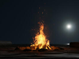 3d rendering of large bonfire with sparks and particles in front of full moon light at sand beach