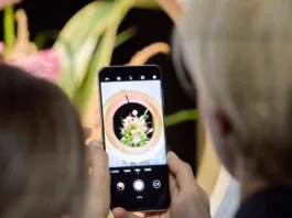 Roka drži telefon, na obeh straneh se vidita glavi