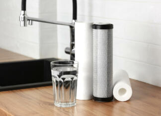 Vodni filter je še kako pomemben pri tvojem zdravju A glass of clean fresh water and set of filter cartridges on wooden table in a kitchen interior. Installation of reverse osmosis water purification system. Concept Household filtration system