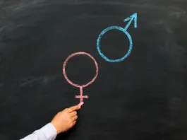 A man's hand with chalk draws a male and female gender symbol on a chalkboard