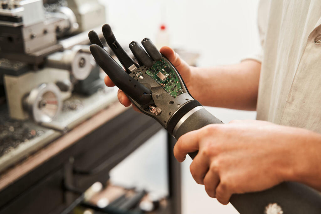 Close up view of the man engineer wearing white robe holding bionic hand while developing prothesis artificial limbs. Engineering of the bionic hands concept. Stock photo
