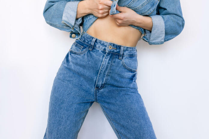 Cropped shot of young slender woman in a fashionable blue jeans with a high fit isolated on a white background. Beauty and fashion concept