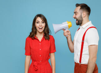 Zakaj dejstva ne spremenijo našega mišljenja? Excited cheerful young couple two friends man woman wearing white red clothes screaming in megaphone isolated on pastel blue color background studio portrait. St. Valentine's Day holiday concept