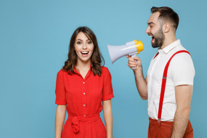 Excited cheerful young couple two friends man woman wearing white red clothes screaming in megaphone isolated on pastel blue color background studio portrait. St. Valentine's Day holiday concept