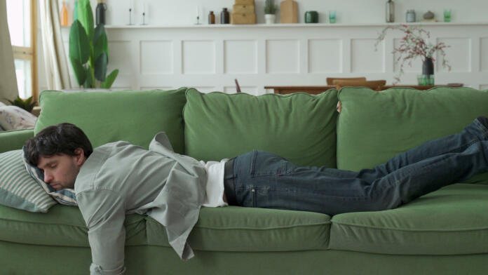 Exhausted young man came home after work flopped down on sofa.